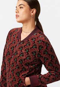 Giacca zip-up bordeaux con motivo a onde multicolori, colletto e polsini a coste, caratterizzata da una texture morbida e tasche laterali.