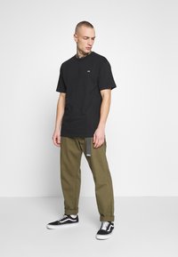 Camiseta negra de manga corta con un pequeño logo, combinada con pantalones cargo verdes y zapatillas negras de caña baja. Ajuste simple y relajado.