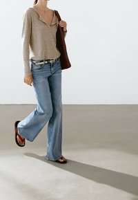 Beige ribbed long-sleeve top, light blue flared jeans, black and red flip-flops, braided brown tote bag. Simple design and relaxed fit.