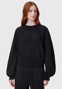 Sudadera negra con cuello redondo, mangas raglán y dobladillo ajustado. Presenta un logo sutil en el pecho y un acabado suave y texturizado.
