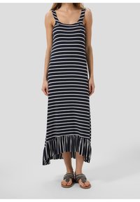 Robe maxi rayée bleu marine avec des rayures blanches, dotée de larges bretelles et d'un ourlet volanté. Portée avec des tongs ornées.