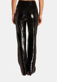 Pantalon noir à sequins avec une coupe évasée, présentant une texture lisse et une surface brillante. La taille est élastique pour plus de confort et un bon ajustement.
