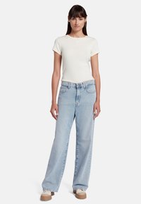 T-shirt blanc à manches courtes avec un petit motif de cœur, associé à un jean ample bleu clair et des baskets à plateforme beiges.