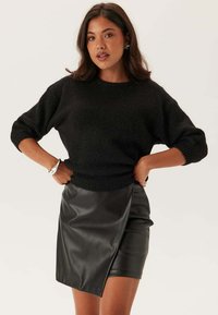 Maglione nero lavorato a maglia con scollatura rotonda e maniche tre quarti, abbinato a una gonna mini aderente in pelle nera con orlo diagonale.