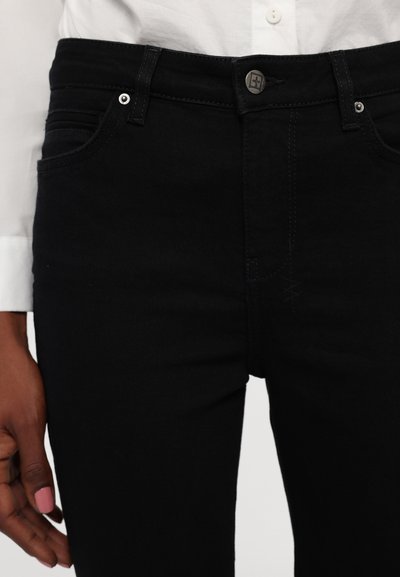 Jeans de mezclilla negra con un corte ajustado, diseño de cinco bolsillos y cierre de botón, con detalles de costura sutiles y acentos de herrajes metálicos.