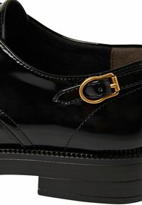 Schwarze Lackleder-Schuh mit runder goldener Schnallendetail und strukturiertem Sohlen mit gesteppten Akzenten. Glatte Oberfläche und strukturierte Form.