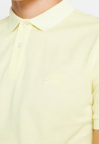 Polo in cotone giallo chiaro con colletto classico, due bottoni e logo ricamato discreto sul petto. Maniche corte.