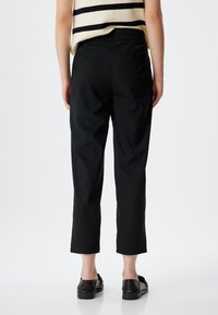 Sorte cropped bukser med en glat tekstur, der har en standard talje og to baglommer. Kombinationen inkluderer sorte slip-on sko.