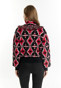 Maglione lavorato a maglia con un design a fantasia in rosso, nero e bianco; presenta un colletto con frange e maniche a spalla abbassata.