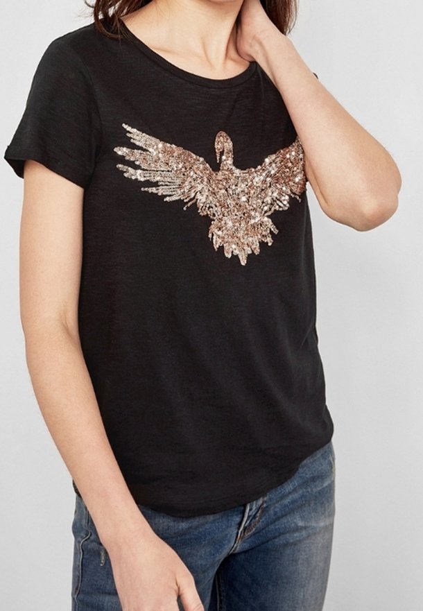Czarna koszulka z krótkim rękawem z aplikacją w postaci cekinowego orła w kolorze różowego złota z przodu. Materiał wydaje się być miękki i ma luźny krój.