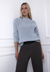 Jasnoniebieski sweter z dzianiny z wysokim kołnierzem i teksturowanym wzorem, zestawiony z szerokimi spodniami w kolorze ciemnobrązowym, posiadającymi gładki pas w talii.