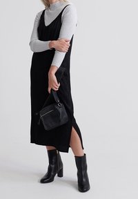 Czarna sukienka na ramiączkach z bocznymi rozcięciami, nałożona na jasnoszary prążkowany golf. Czarne botki na obcasie i mała teksturowana torebka do noszenia na krzyż.