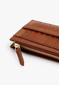 Cartera de cuero marrón con un acabado texturizado, que presenta un zipper dorado y una pequeña lengüeta de cuero. Diseño de rayas horizontales en relieve.