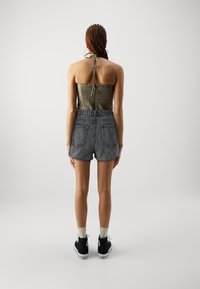 Černé džínové šortky s třásněmi, spárované s přiléhavým halter topem olivově zelené barvy s texturovaným zadním dílem. Nosené s černými teniskami a ponožkami.