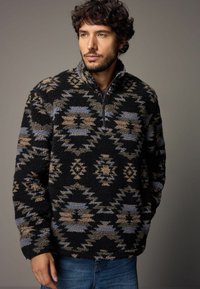 Czarny polarowy sweter z pół zamkiem, zdobiony skomplikowanymi geometrycznymi wzorami w beżowym i niebieskim kolorze. Miękka faktura i luźny krój.