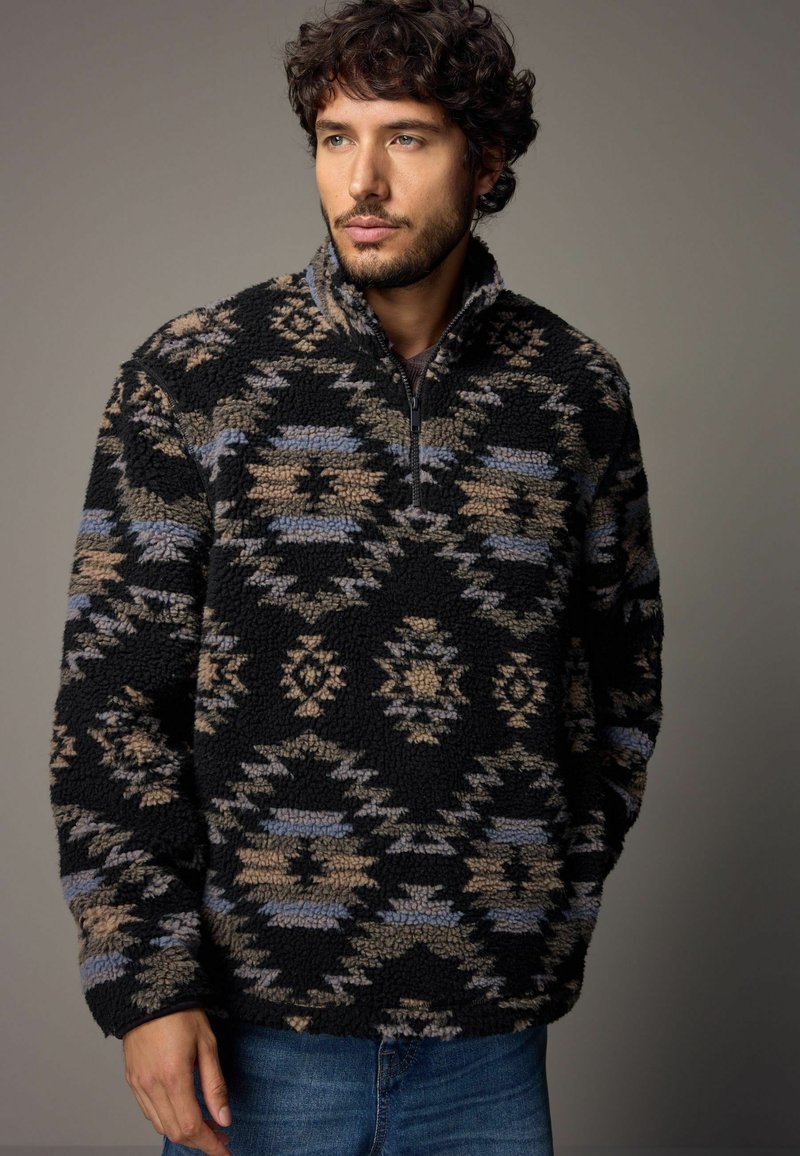 Czarny polarowy sweter z pół zamkiem, zdobiony skomplikowanymi geometrycznymi wzorami w beżowym i niebieskim kolorze. Miękka faktura i luźny krój.