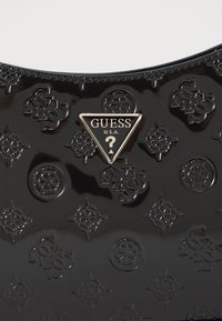 Sort patentlæder taske med prægede mønstre og et guldtriangel logo med "GUESS U.S.A." i midten. Glat, blank tekstur.
