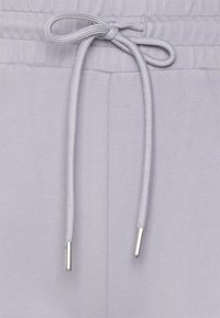 Light gray pants with a drawstring waist featuring silver tips on the ends of the drawstrings, showcasing a smooth fabric texture.