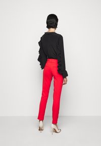 Czarna bluzka z falbaniastymi rękawami, w połączeniu z dopasowanymi czerwonymi spodniami i beżowymi butami na wysokim obcasie. Prosty fason i gładkie faktury.