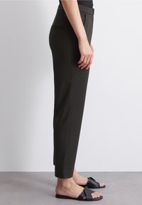 Pantalon tailored vert foncé avec une coupe droite, poches latérales et couture visible. Assorti à des sandales plates noires. Texture lisse.