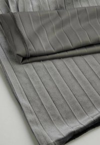 Szara tkanina o gładkiej fakturze, z pionowymi żebrowanymi wzorami. Zagięty brzeg prezentuje przeszyty szew. Ogólnie wygląda miękko i puszyście.