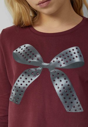 Bordeaux-rotes Langarmhemd mit einem grauen Schleifengrafik und lila Strasssteinen, die dem Design Textur und Detail verleihen. Glatte Stoffoberfläche.