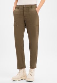 Pantalon cargo kaki avec plusieurs poches avant, coupe ajustée et texture lisse. Associé à des bottes à lacets de couleur claire.