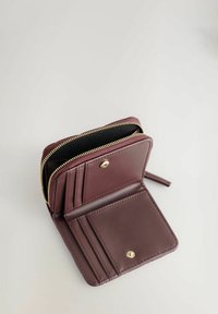 Portefeuille en cuir bordeaux avec fermeture éclair dorée, comportant deux compartiments, plusieurs emplacements pour cartes et une fermeture à pression. L'intérieur est tapissé de noir.
