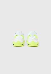 Αθλητικά παπούτσια με υφή λευκό επάνω μέρος, φωτεινές νέον κίτρινες λεπτομέρειες στη φτέρνα και μια μαλακή σόλα με σκοτεινές λεπτομέρειες.