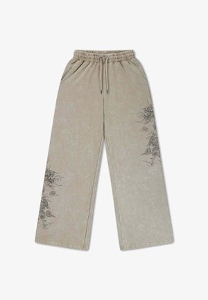 Pantaloni beige a gamba larga con vita elastica e coulisse, con elaborati disegni di draghi neri sulla coscia sinistra e sul polpaccio destro.
