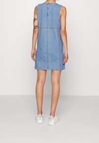 Denim ärmlös klänning med rak skärning, med synlig sömnad och en slits bak. Enfärgad ljusblå färg. Matchas med flerfärgade sneakers.