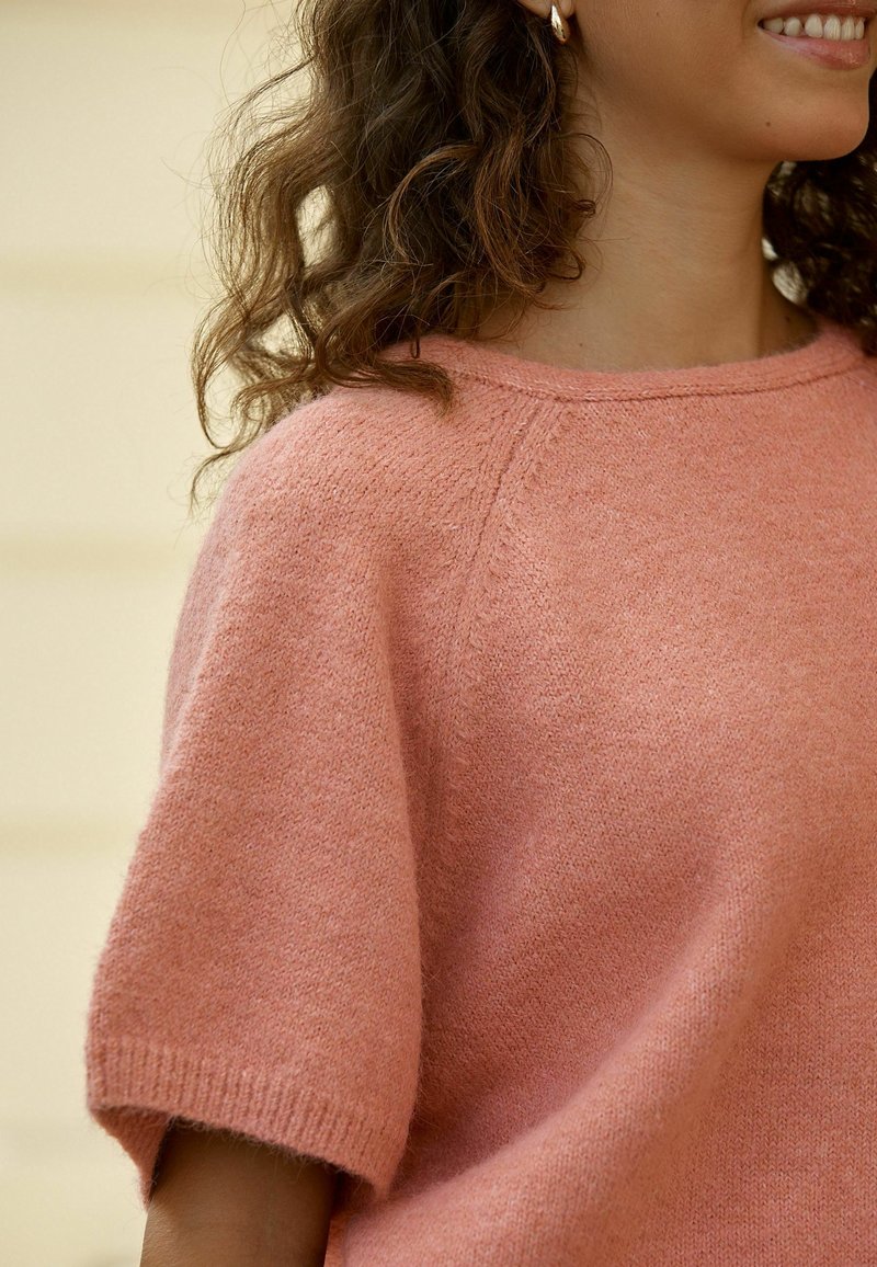 Kurzärmeliger Pullover mit Rundhalsausschnitt aus zartem rosa Strick, mit leicht lockerer Passform und gerippten Bündchen, akzentuiert durch eine strukturierte Oberfläche.