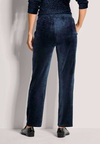 Marineblaue Samthose mit glatter Textur und geradem Bein Design. Verfügt über einen bequemen Bund und wird mit schwarzen Lackschuhen getragen.