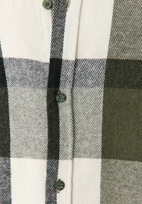 Gros plan d’un tissu à carreaux noir, blanc et gris avec des coutures visibles et trois boutons foncés le long de la couture centrale.