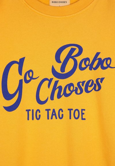 Felpa gialla con grande testo blu: "Vai Bobo Choses TIC TAC TOE." Tessuto morbido e dettaglio del collo a coste. Design informale.