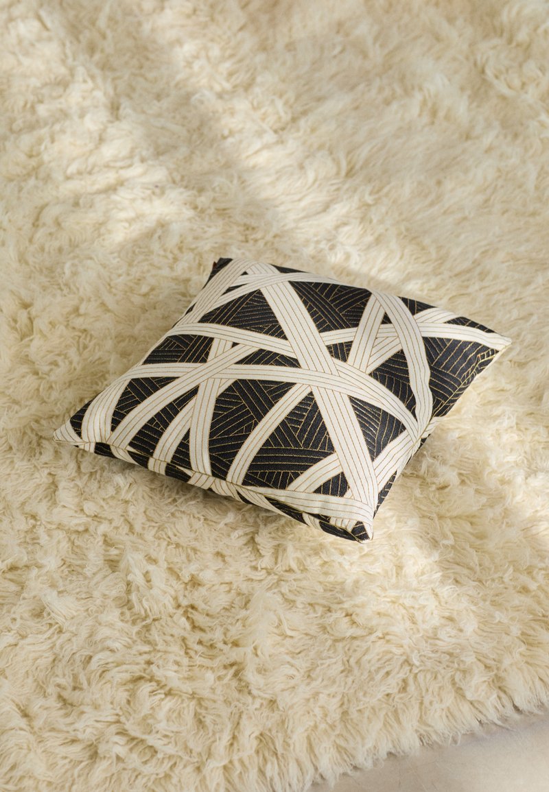 Black and cream decorative pillow with a geometric pattern, featuring woven textures, placed on a fluffy beige rug.