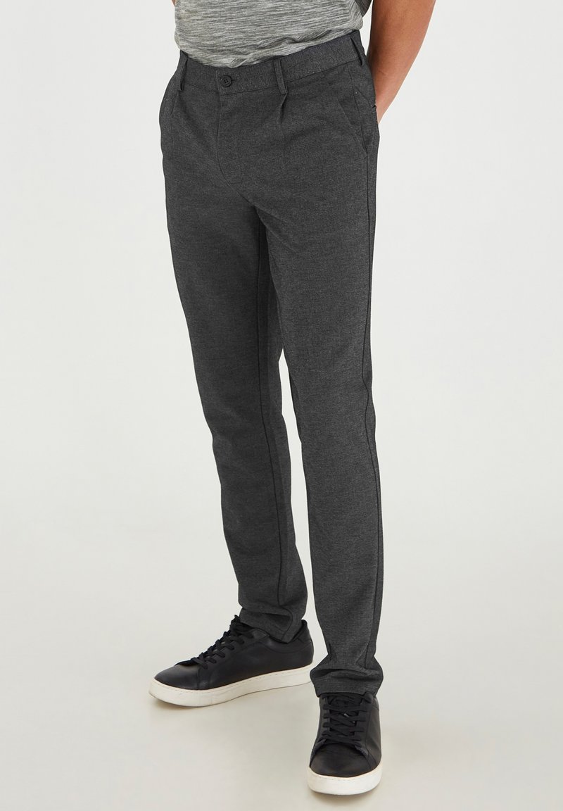 Pantalones gris oscuro de corte slim con una tela texturada, que cuentan con bolsillos laterales y detalles en negro. Combinados con zapatillas negras.