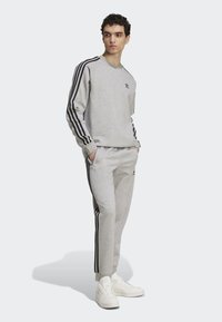 Grå sweatshirt og bukser med sorte sidelabber, ribbede manchetter og et lille logo. Bruges med hvide sneakers, der viser et afslappet fit.