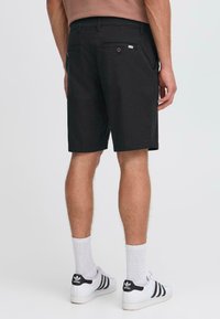 Black shorts made of cotton, featuring a straight cut with two back pockets and a small label. Worn with white sneakers and socks.