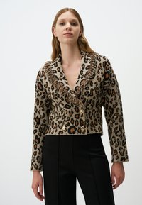 Cardigan cropped in stampa leopardata beige e nera con accenti arancioni, presenta un colletto frangiato e doppio bottone dorato. Materiale in maglia testurizzata.