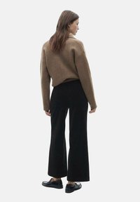 Brown knit sweater with a loose fit, paired with high-waisted black wide-leg pants. Smooth fabric texture and flat shoes.