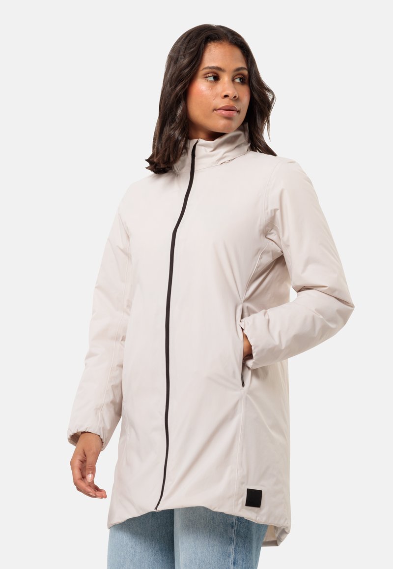 Helles beige langes Jacket mit schwarzem Reißverschluss, Seitentaschen, hohem Kragen und weicher Textur. Verfügt über einen quadratischen schwarzen Akzent am Saum.