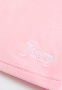 Mekana ružičasta tkanina s bijelim vezom riječi "Juicy" i vidljivim ušivenim šavom duž ruba.