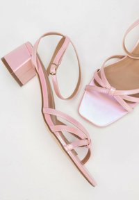 Roze sandalen met bandjes, een vierkante neus, glanzende afwerking en een bescheiden blokhak. Bevat meerdere kruisende banden en een enkelgesp.