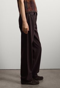 Donkerbruine wijde broek van een gestructureerd materiaal, met zijzakken en een relaxte pasvorm. In combinatie met donkerbruine schoenen voor contrast.