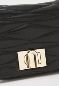 Borsa in pelle nera con texture trapuntata, dotata di una chiusura in metallo dorato con il logo "Furla". Tra i dettagli si notano le cuciture visibili.