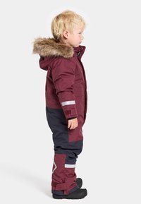 Vinröd och marinblå vadderad overall med huva fodrad med konstgjord päls, reflekterande detaljer och justerbara ärmar. Har robust material och hållbara stövlar.