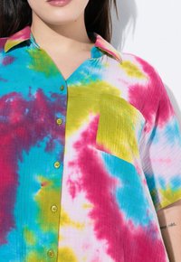Maglietta tie-dye multicolore con motivi blu, rosa e verde, maniche corte, colletto e tasca sul petto con texture verticale.