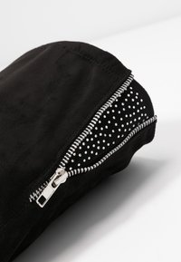 Sacchetto in suede nero con zip in tonalità argento, con un interno testurizzato e chiodato e forma arrotondata. Design semplice, finitura opaca liscia.