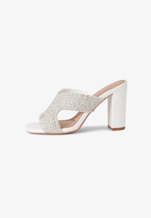 Sandale blanche à talon ouvert, avec larges brides scintillantes en strass et talon bloc, sur fond blanc.